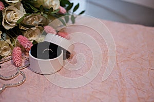 Engagement ring in a round white box on a pink paper background and with a bouquet of white roses and a lagurus