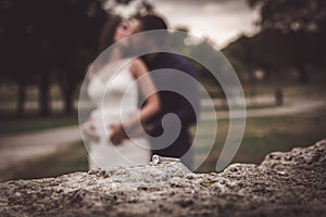 Engagement ring on the stone surface with blurred bride and groom in backround