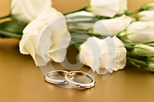 Two golden wedding rings with white roses on a gold background stock images