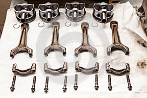 Engine connecting rods and pistons used and removed from a four-cylinder engine on a white soft cloth in a vehicle repair workshop