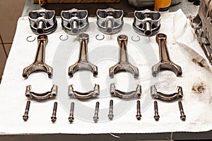 Engine connecting rods and pistons used and removed from a four-cylinder engine on a white soft cloth in a vehicle repair workshop