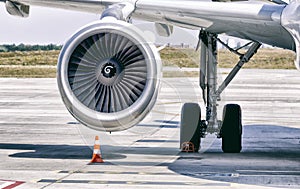 Engine of modern passenger jet airplane. Rotating fan and turbine blades. Traffic cone near it. Landing gear. Close-up front view.