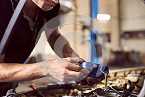 Engine oil changing in auto workshop. Focus on pouring grease from bottle by repairman hands. Maintenance car engine