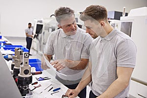 Engineer And Apprentice Discussing Job Sheet In Factory