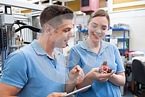 Engineer And Apprentice Examining Component In Factory