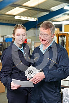 Engineer And Apprentice Looking At Component In Factory