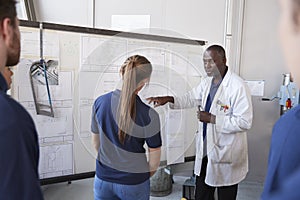 Engineer with apprentice at white board in front of group