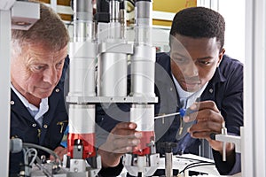 Engineer And Apprentice Working On Machine In Factory