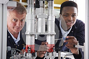 Engineer And Apprentice Working On Machine In Factory