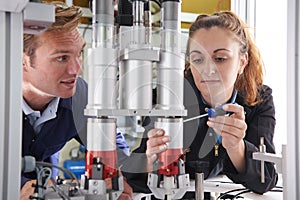 Engineer And Apprentice Working On Machine In Factory