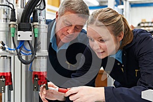 Engineer And Apprentice Working On Machine In Factory