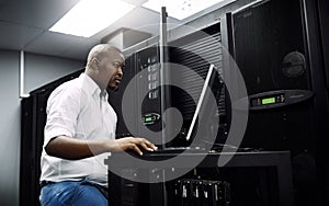 Engineer, black man or coding on laptop in server room for big data, network glitch or digital website. Code, IT support