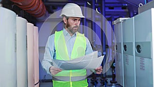 Engineer with blueprint in factory boiler room. Worker inspects equipment.