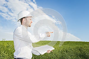 Engineer builder with drawings in his hands points to construction site of building. geologist on a green meadow in the afternoon