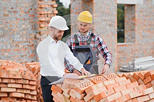 engineer and builder in hard hats discussing blueprint on construction site.