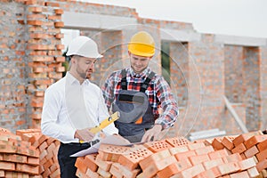 engineer and builder in hard hats discussing blueprint on construction site.