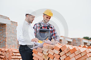 engineer and builder in hard hats discussing blueprint on construction site.