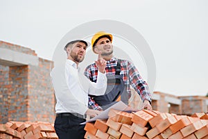 engineer and builder in hard hats discussing blueprint on construction site.