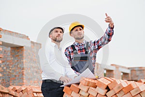 engineer and builder in hard hats discussing blueprint on construction site.