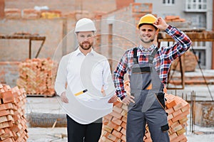 engineer and builder in hard hats discussing blueprint on construction site.