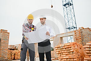 engineer and builder in hard hats discussing blueprint on construction site.