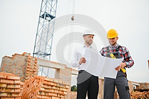 engineer and builder in hard hats discussing blueprint on construction site.