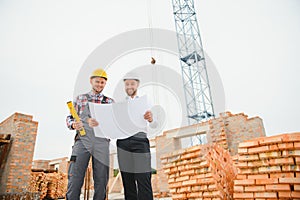 engineer and builder in hard hats discussing blueprint on construction site.