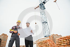 engineer and builder in hard hats discussing blueprint on construction site.