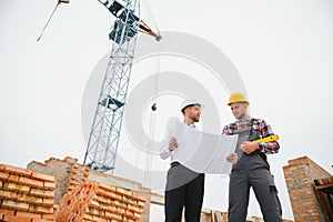 engineer and builder in hard hats discussing blueprint on construction site.