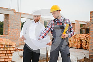 engineer and builder in hard hats discussing blueprint on construction site.