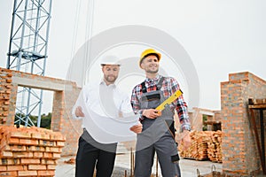 engineer and builder in hard hats discussing blueprint on construction site.