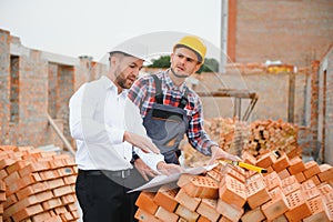 engineer and builder in hard hats discussing blueprint on construction site.