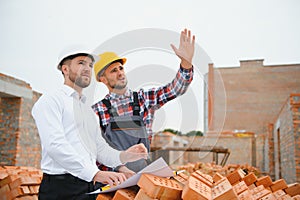 engineer and builder in hard hats discussing blueprint on construction site.