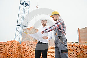 engineer and builder in hard hats discussing blueprint on construction site.