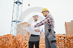 engineer and builder in hard hats discussing blueprint on construction site.