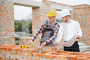 engineer and builder in hard hats discussing blueprint on construction site.