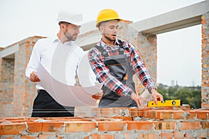 engineer and builder in hard hats discussing blueprint on construction site.