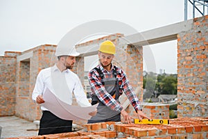 engineer and builder in hard hats discussing blueprint on construction site.