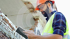 An engineer builder in a helmet is calculating the building demolition plan and looking at the construction project on a