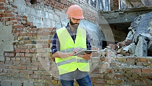 An engineer builder in a helmet is calculating the building demolition plan and looking at the construction project on a