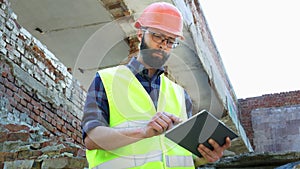 An engineer builder in a helmet use tablet, building demolition plan and looking at the construction project