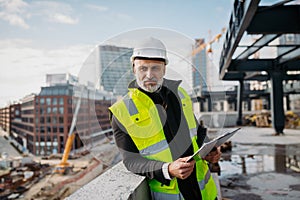 Engineer checking building documentation on clipboard at construction site.