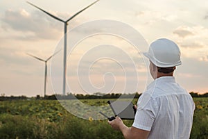 Engineer is checking energy production on wind turbine. Worker in windmills park in helmet and with tablet