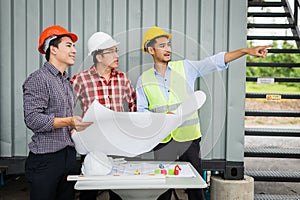 Engineer and construction team holding blueprint and pointing finger to building.