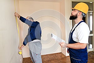 Engineer, contractor and project manager with his colleague, construction worker, handyman and builder is measuring wall of room.