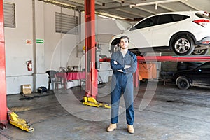 Engineer In Coveralls Standing Arms Crossed Against Car Lift