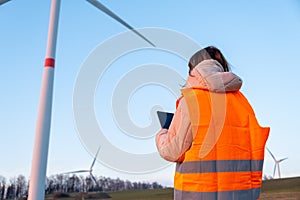 Engineer does maintenance and repairs wind wills or wind turbine using a tablet in the orange vesta.