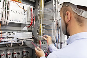 Engineer electrician with multimeter in electrical control box tests equipment. Maintenance of electrical panel