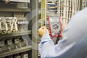 Engineer electrician with multimeter in hands at electric automation box panel. Service engineer tests circuit of industrial