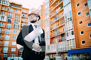 Engineer in front of modern building with plan looking at blueprint